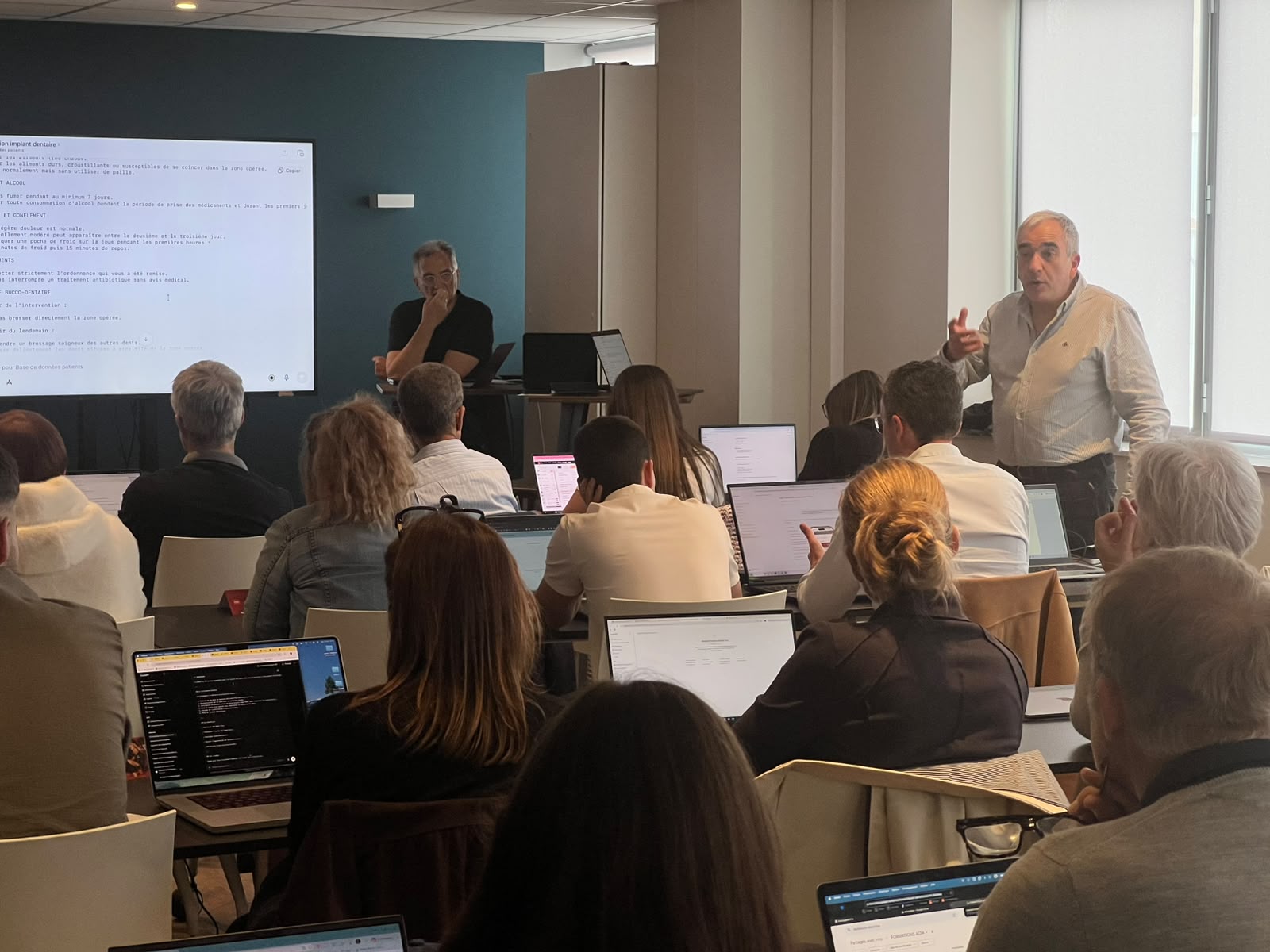 Session ADIA : les deux formateurs présentent la rédaction assistée par IA des consignes post-opératoires devant un groupe de chirurgiens-dentistes.